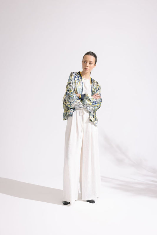 Person wearing a colorful floral jacket and white pants on a white background