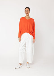 Woman wearing an orange top and white pants on a white background