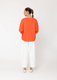 Person wearing an orange top and white pants on a white background