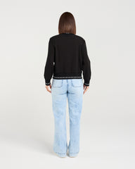 Person wearing a black sweater and light blue jeans on a white background