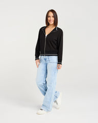 Woman wearing a black jacket with studded details and light blue jeans on a white background