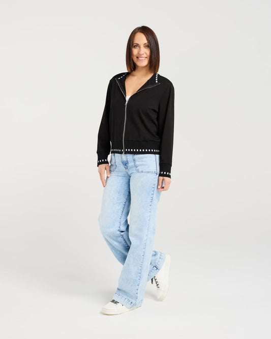 Woman wearing a black jacket with studded details and light blue jeans on a white background