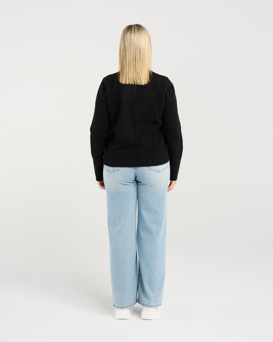 Person wearing a black sweater and light blue jeans on a white background