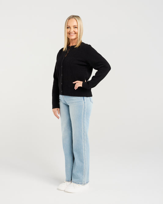 Woman wearing a black cardigan and light blue jeans on a white background
