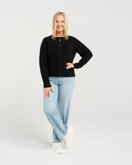 Woman wearing a black cardigan, light blue jeans, and white sneakers on a white background