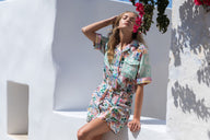 Woman in a colorful dress standing against a white wall with flowers.