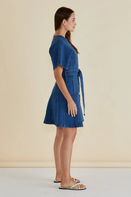 Woman wearing a blue denim dress against a beige background