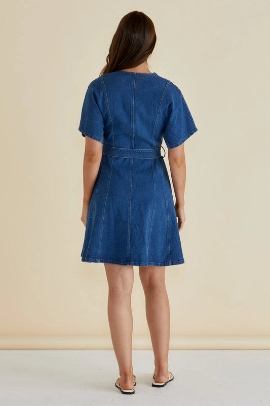 Woman wearing a blue denim dress against a beige background