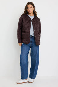 Woman wearing a brown quilted jacket, gray shirt, blue jeans, and white sneakers on a white background