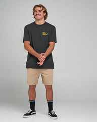 Man wearing a black t-shirt with a logo and beige shorts on a gray background