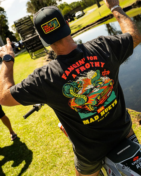 Person wearing a black t-shirt with colorful graphics and text, standing outdoors near water.