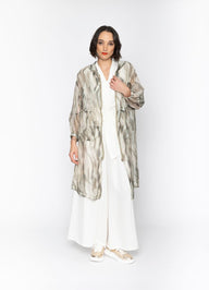 Woman wearing a long, patterned coat over a white outfit on a white background