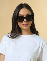 Woman wearing dark sunglasses and a white shirt against a beige background