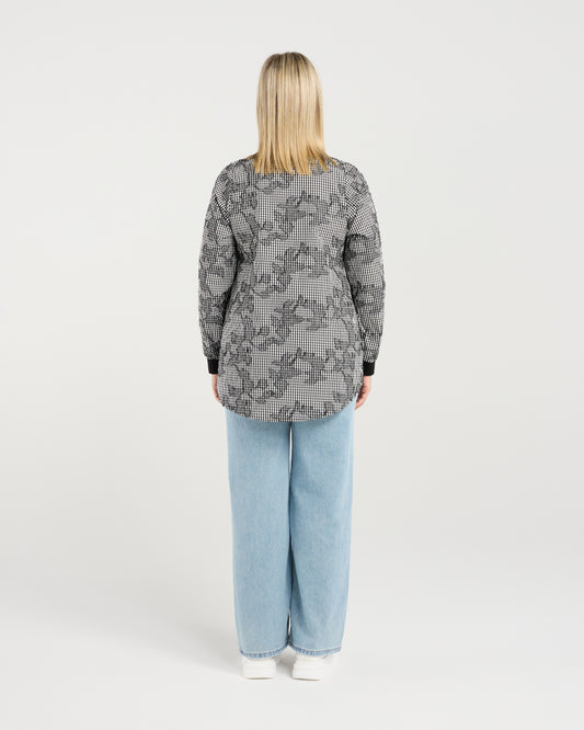 Person wearing a patterned shirt and light blue jeans on a white background