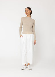 Woman wearing a beige sweater and white pants on a white background