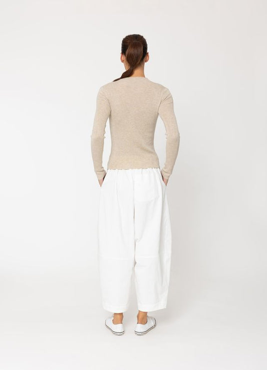 Person wearing a beige sweater and white pants on a white background