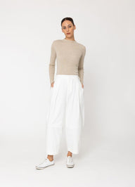 Woman wearing a beige sweater and white pants on a white background