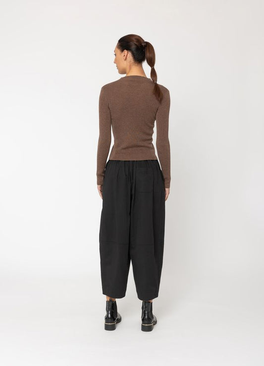 Person wearing a brown long-sleeve top and black pants on a white background