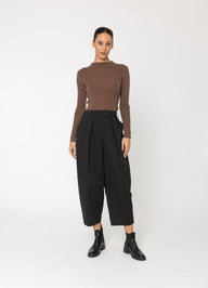 Woman wearing a brown sweater and black pants on a white background