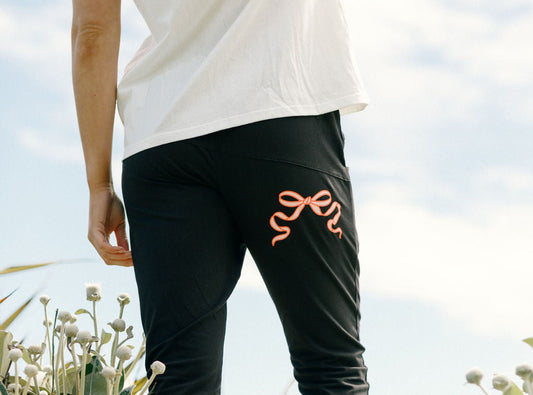 Person wearing Lady wearing Home-Lee Apartment Pants with pink Bow, white sneakers, standing in a natural setting with plants and sky.