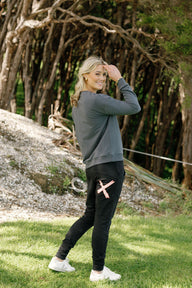 Woman in gray sweatshirt and black pants standing outdoors with trees in the background