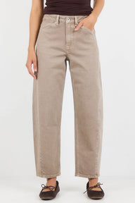 A person wearing light beige wide-leg cropped jeans with a dark brown top and dark brown flat shoes, standing against a plain white studio background.