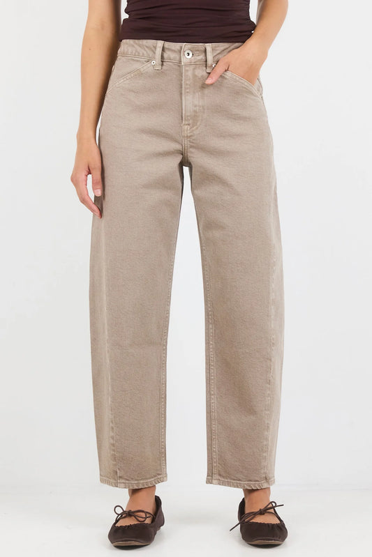 A person wearing light beige wide-leg cropped jeans with a dark brown top and dark brown flat shoes, standing against a plain white studio background.