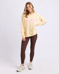 Woman wearing a yellow sweatshirt with pink text and brown leggings on a white background