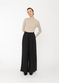 Woman wearing a beige sweater and black wide-leg pants on a white background