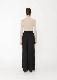 Person wearing a beige top and black wide-leg pants on a white background