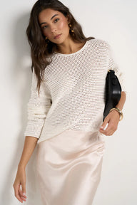 Woman wearing a textured white top and satin skirt against a plain background