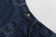Close-up of blue denim overalls with a button on a light gray background