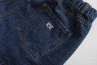 Close-up of blue jeans with a logo on the pocket against a light gray background