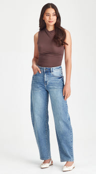 Woman wearing a sleeveless brown top and light blue jeans on a white background