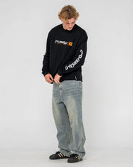 Person wearing a black long-sleeve shirt with logos and light blue jeans on a white background