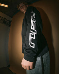 Person wearing a black hoodie with a white logo against a plain wall.