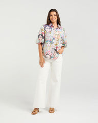 Woman wearing a floral blouse and white pants on a white background