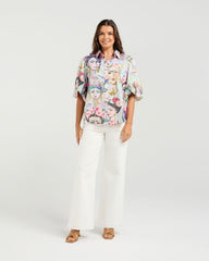 Woman wearing a floral blouse and white pants on a plain background