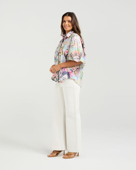Woman wearing a floral blouse and white pants on a plain background