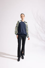 Person wearing a floral blouse, navy sweater, and black pants on a white background
