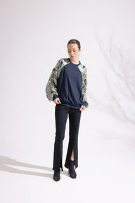 Person wearing a navy sweater with floral sleeves and black pants on a white background