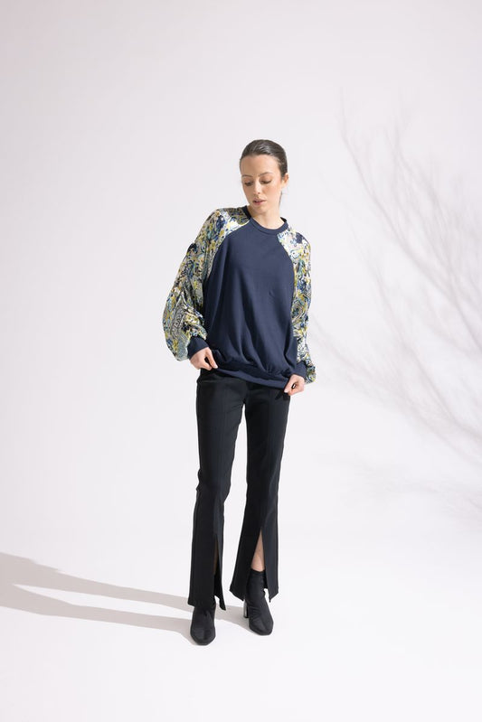 Person wearing a navy sweater with floral sleeves and black pants on a white background