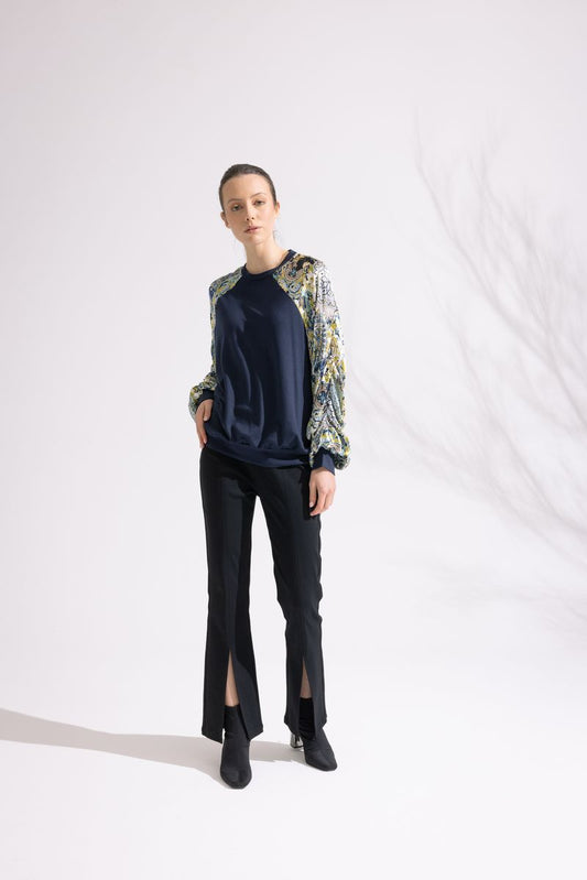 Person wearing a navy sweater with floral sleeves and black pants on a white background