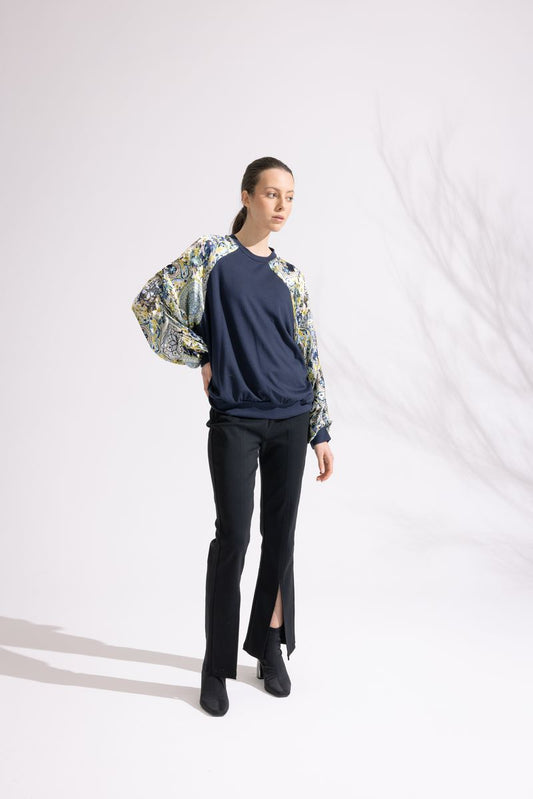 Woman wearing a navy sweater, black pants, and a floral jacket on a white background