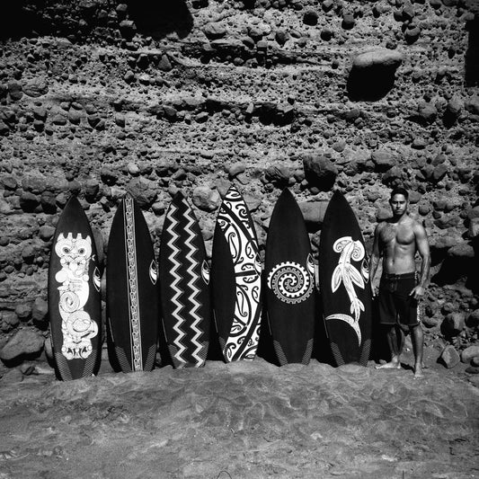 Man standing next to five surfboards with tribal designs against a rocky background