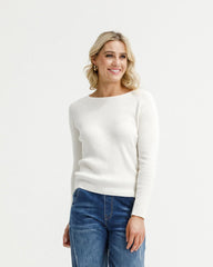 Woman wearing a white sweater and blue jeans on a plain background