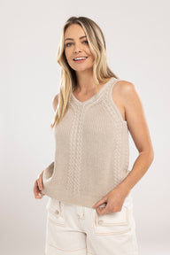 Woman wearing a beige knitted sleeveless sweater against a white background