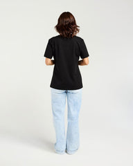 A woman viewed from behind wearing a plain black short-sleeve t-shirt and light-wash blue jeans against a clean white studio background.