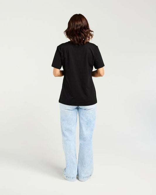 A woman viewed from behind wearing a plain black short-sleeve t-shirt and light-wash blue jeans against a clean white studio background.