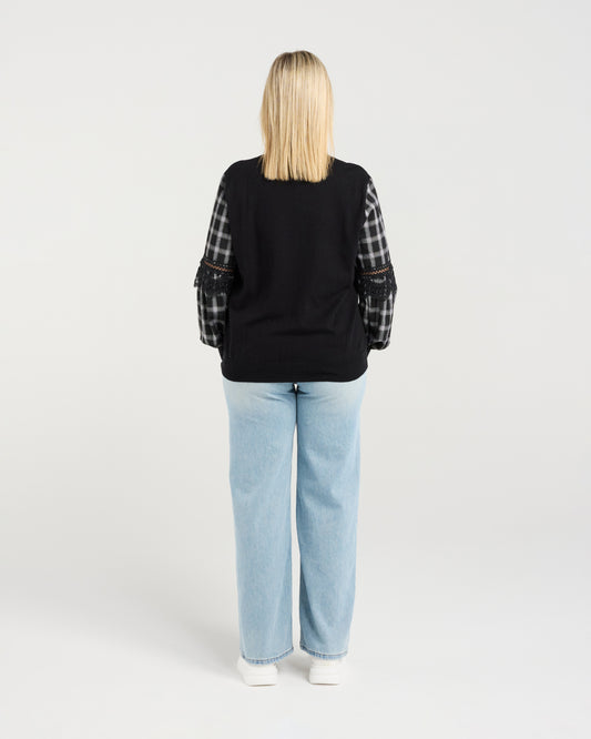 Person wearing a black sweater with plaid sleeves and light blue jeans on a white background